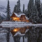 wooden house near pine trees and pond coated with snow during daytime